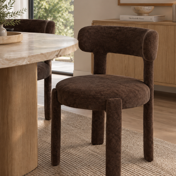 Silla tapizada marrón para comedor con asiento curvo, respaldo acolchado redondeado y patas tapizadas a juego.